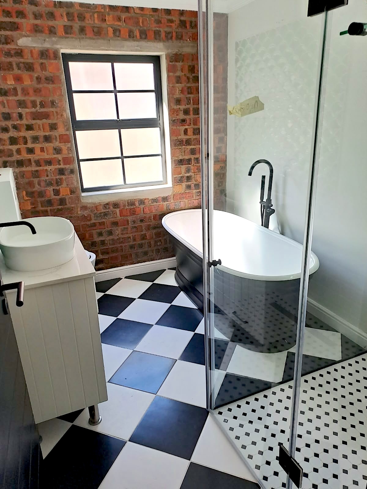 Bathroom with checkerboard floor, exposed brick and freestanding bath